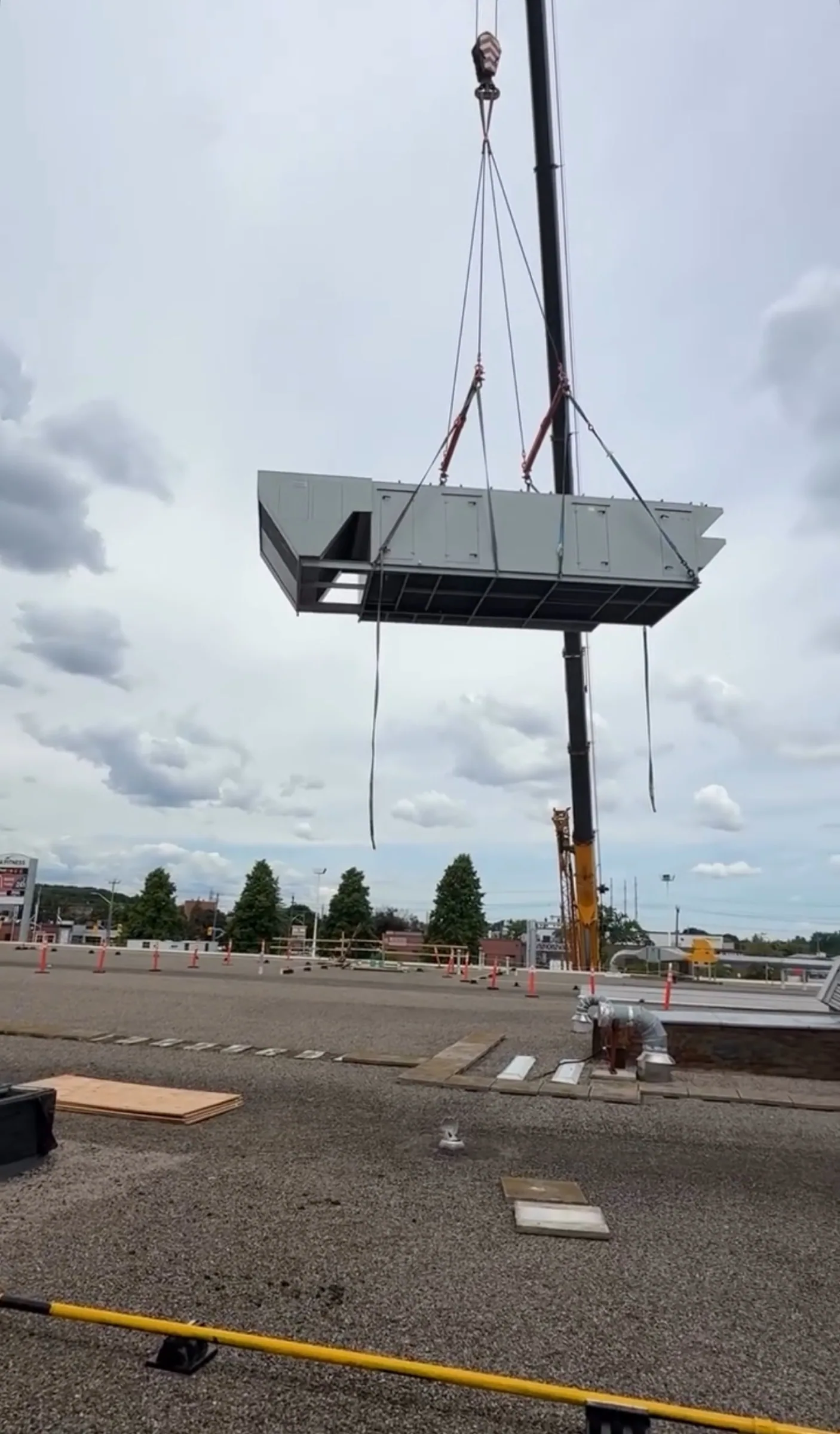 Rooftop mechanical unit suspended on a crane line above a commercial building