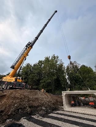 Crane setting a precast concrete structure beside an open excavation